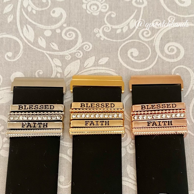 K&ouml;nnte beinhalten: Drei Uhrenarmb&auml;nder mit austauschbaren Charms. Die Charms sind silber, gold und ros&eacute;gold und haben die Worte "Blessed" und "Faith" eingraviert. Die Charms sind mit kleinen Strasssteinen verziert.