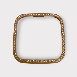 May include: A gold-toned square watch band with a clear rhinestone border.
