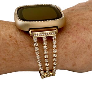 May include: Gold-tone watch band with a crystal-encrusted design. The band is made of metal and has a three-row design with clear crystals.