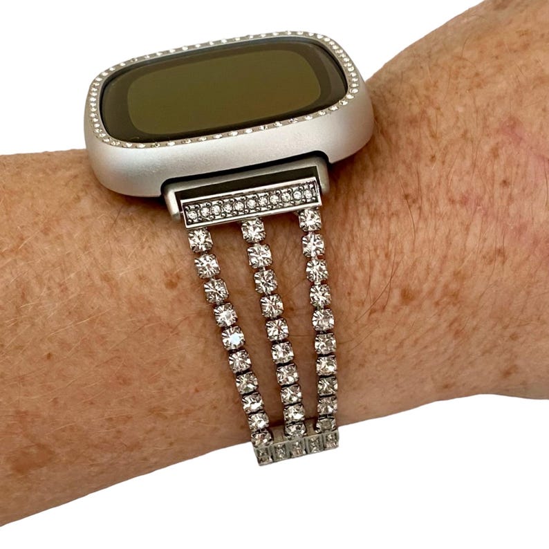 May include: Silver smartwatch with a clear crystal rhinestone band. The band is made of three rows of rhinestones.