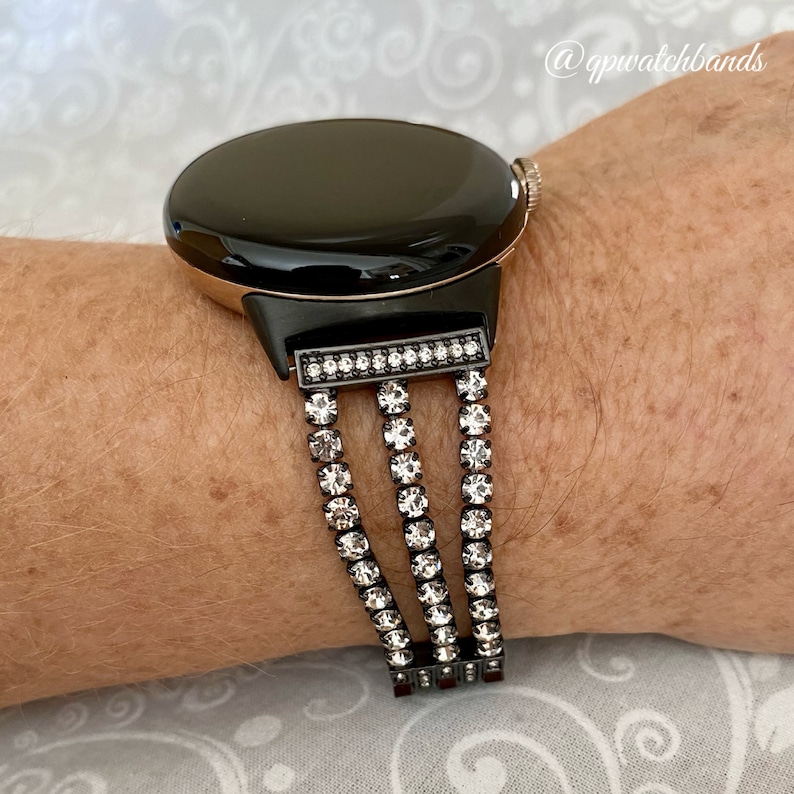 Pu&ograve; includere: Un orologio intelligente nero con una lunetta in oro rosa e un cinturino nero e strass. Il cinturino ha tre file di strass.