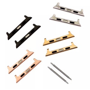 May include: An assortment of watch band adapters in black, silver, gold, and rose gold. The adapters have a rectangular shape with a central oval opening and are designed to connect to a watch band. Two spring bars are also included.
