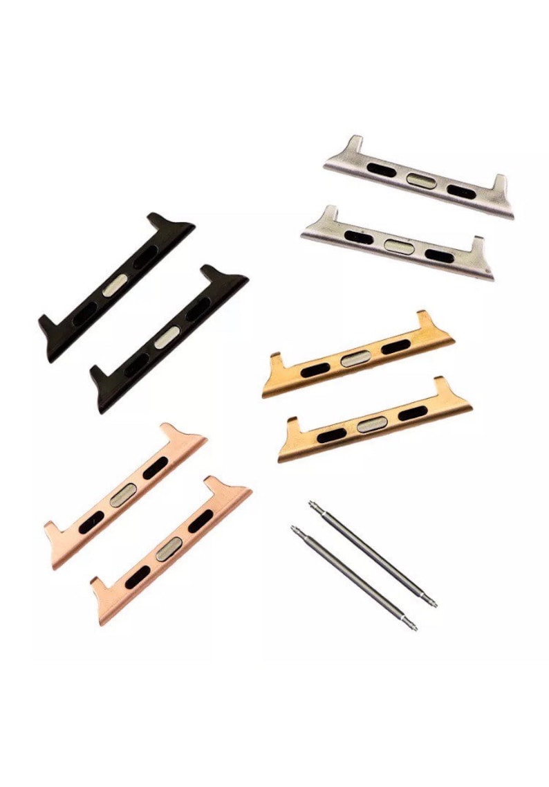 May include: An assortment of watch band adapters in black, silver, gold, and rose gold. The adapters have a rectangular shape with a central oval opening and are designed to connect to a watch band. Two spring bars are also included.