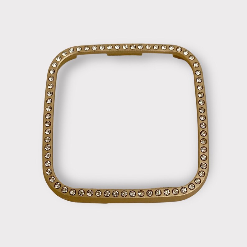 May include: Gold-toned square watch band with a clear crystal embellishment around the edge.