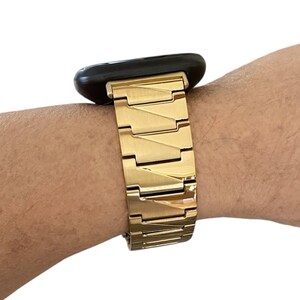 K&ouml;nnte beinhalten: Ein goldfarbenes Metall-Uhrenarmband mit einem schwarzen Zifferblatt. Das Armband besteht aus rechteckigen Gliedern, die miteinander verbunden sind. Die Uhr befindet sich an einem Handgelenk.