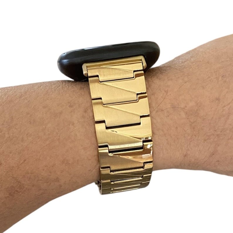 K&ouml;nnte beinhalten: Ein goldfarbenes Metall-Uhrenarmband mit einem schwarzen Zifferblatt. Das Armband besteht aus rechteckigen Gliedern, die miteinander verbunden sind. Die Uhr befindet sich an einem Handgelenk.