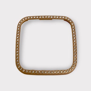 May include: A gold-toned square watch band with a clear rhinestone border.