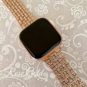 以下が含まれることがあります： ローズゴールドのApple Watchバンド。クリアなラインストーンが全面に敷き詰められています。バンドは金属製で、留め具が付いています。