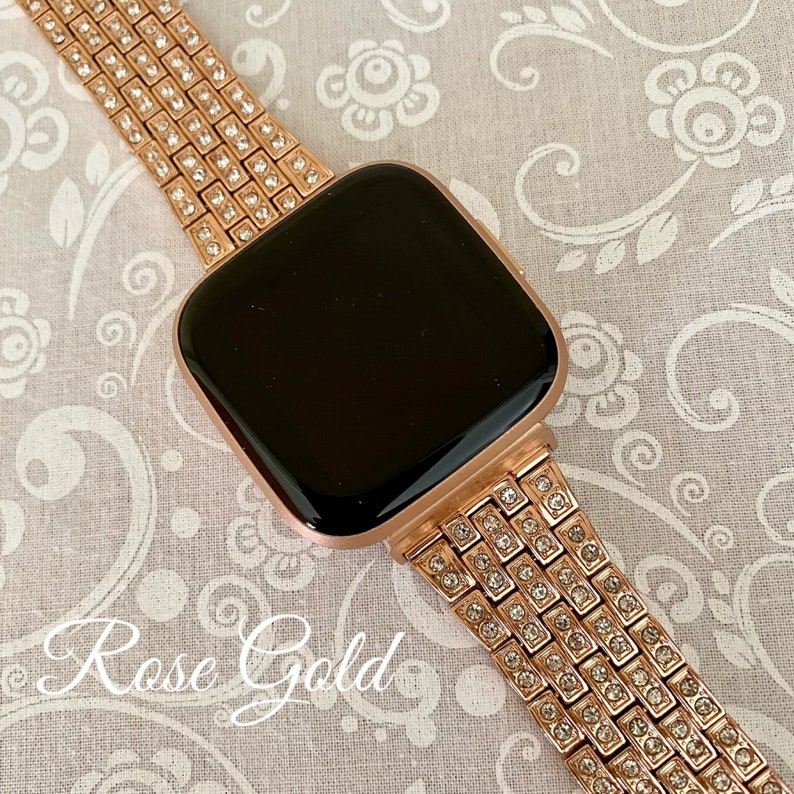 以下が含まれることがあります： ローズゴールドのApple Watchバンド。クリアなラインストーンが全面に敷き詰められています。バンドは金属製で、留め具が付いています。