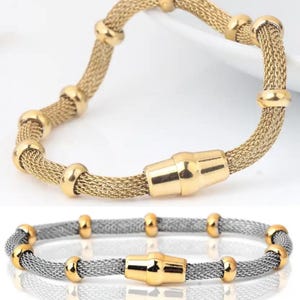 May include: Two bracelets: one gold-toned and one silver-toned. Both feature a mesh design with gold-colored accents and a magnetic clasp. The gold bracelet has gold-colored beads, while the silver bracelet has gold-colored beads.