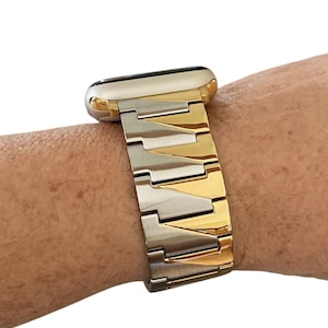 Puede incluir: Una correa de reloj de dos tonos con un acabado plateado y dorado. La correa está hecha de eslabones metálicos y está unida a una esfera de reloj con un bisel dorado. El reloj está en una muñeca.