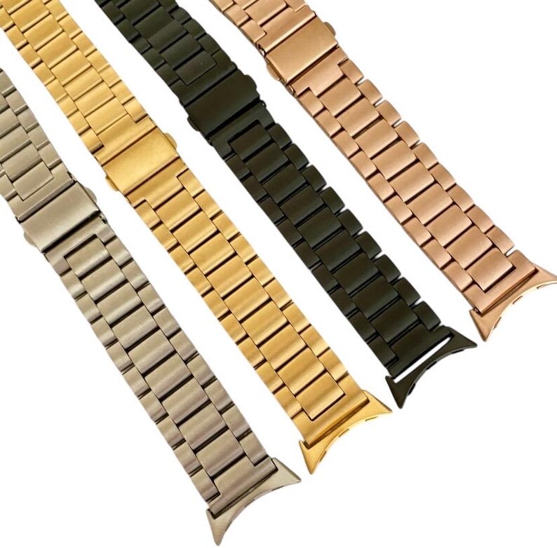 May include: Four metal watch bands in different colors: silver, gold, rose gold, and black. The bands are all the same style, with a brushed finish and a slightly curved shape.