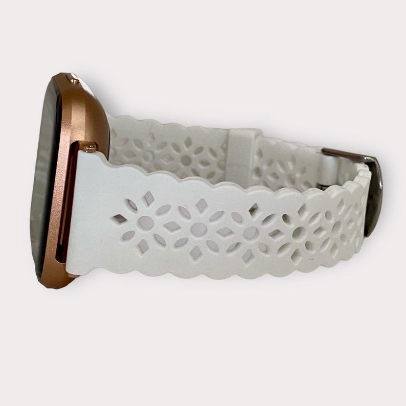 May include: White silicone watch band with a delicate floral pattern. The band has a scalloped edge and a silver buckle.