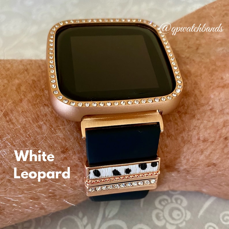 May include: A rose gold watch face with a diamond-encrusted bezel. The watch band is black silicone with a white and black leopard print band and a row of diamonds.