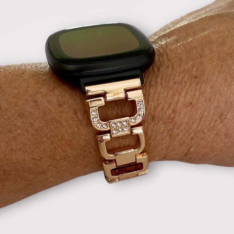 May include: A gold-tone watch band with clear rhinestones. The band is made of metal links and has a polished finish.