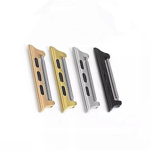 May include: Four watch band adapters in gold, yellow gold, silver, and black. Each adapter has a rectangular shape with rounded edges and a metal bar for attaching to a watch band. The adapters are angled slightly.