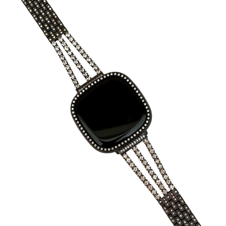 May include: A black smartwatch with a black band adorned with rows of clear rhinestones. The watch face is square and has a black background.