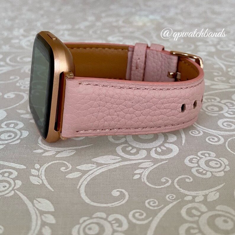 May include: A pink leather watch band with a rose gold watch face. The band has a textured finish and a buckle closure.