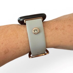 Peut inclure: Un bracelet de montre gris clair avec une boucle en or rose et un accent d&eacute;coratif en cristal. Le cadran de la montre est noir. Le bracelet est fix&eacute; au poignet.