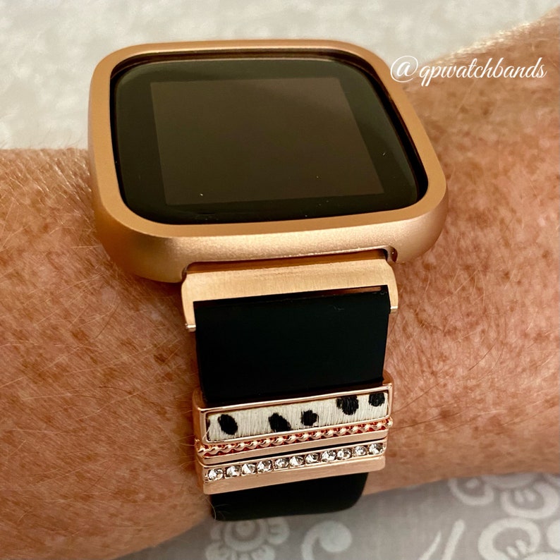May include: Rose gold smartwatch with a black silicone band and a decorative band with a white and black animal print and rhinestones. The watch face is black and the watch is on a person's wrist. @qpiwatchbands