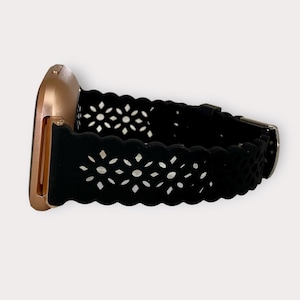 May include: A black silicone watch band with a cut-out floral design. The band is attached to a rose gold smartwatch.