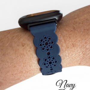 May include: Navy blue watch band with a floral cutout design. The band is attached to a black smartwatch. The text "Navy Blue" is written in cursive at the bottom of the image.