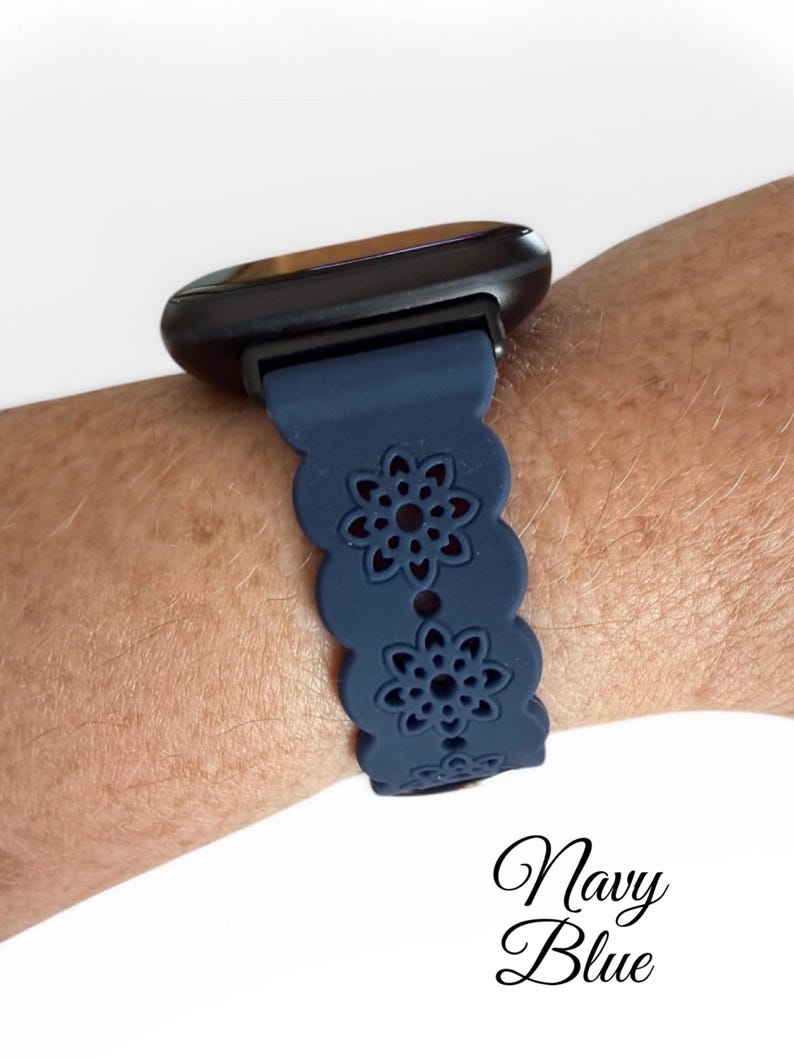 May include: Navy blue watch band with a floral cutout design. The band is attached to a black smartwatch. The text "Navy Blue" is written in cursive at the bottom of the image.