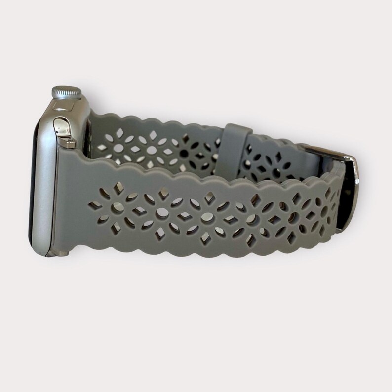May include: A gray silicone Apple Watch band with a delicate floral pattern. The band has a scalloped edge and is designed for a modern look.