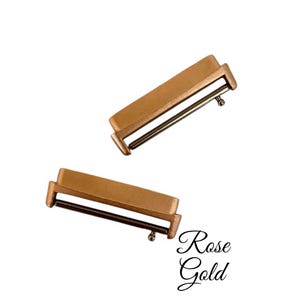 Pu&ograve; includere: Due fibbie per cinturino da orologio in oro rosa. Le fibbie sono rettangolari con un perno metallico che scorre attraverso un foro.