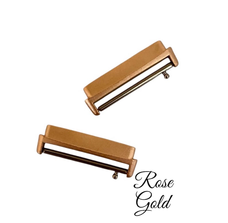 Pu&ograve; includere: Due fibbie per cinturino da orologio in oro rosa. Le fibbie sono rettangolari con un perno metallico che scorre attraverso un foro.