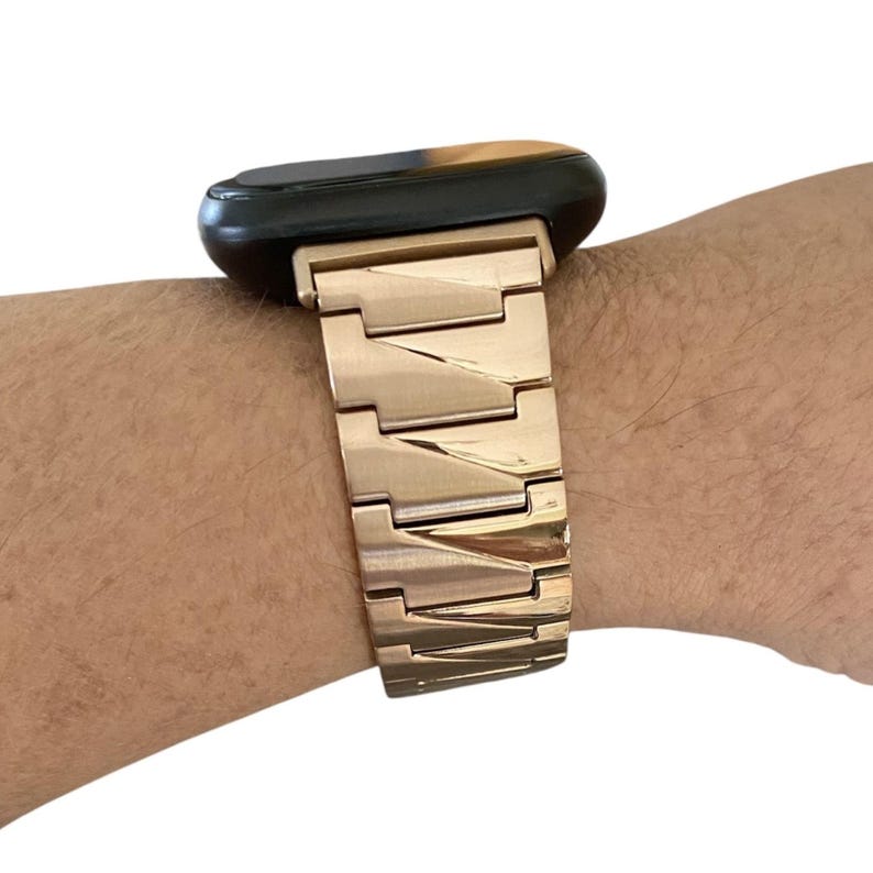 K&ouml;nnte beinhalten: Ein goldfarbenes Metall-Uhrenarmband, das an einem schwarzen und braunen Zifferblatt befestigt ist. Das Armband besteht aus rechteckigen Gliedern. Die Uhr befindet sich am Handgelenk einer Person.