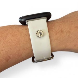 Peut inclure: Bracelet de montre blanc avec une boucle argent&eacute;e et un grand accent en cristal clair et rond. Le bracelet est fix&eacute; &agrave; un cadran de montre noir.