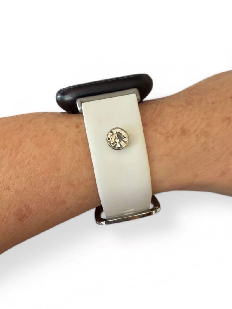 Peut inclure: Bracelet de montre blanc avec une boucle argent&eacute;e et un grand accent en cristal clair et rond. Le bracelet est fix&eacute; &agrave; un cadran de montre noir.