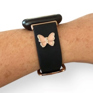 May include: Black watch band with a rose gold buckle and a pink butterfly charm. The butterfly is embellished with small, clear crystals. The watch face is black.
