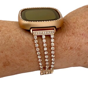 May include: Rose gold smartwatch with a crystal-encrusted band. The watch face is square and has a black screen.