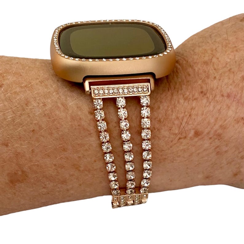 May include: Rose gold smartwatch with a crystal-encrusted band. The watch face is square and has a black screen.