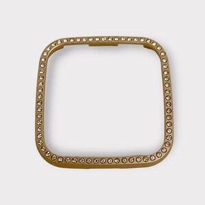 May include: Gold-toned square watch band with a clear crystal embellishment around the edge.