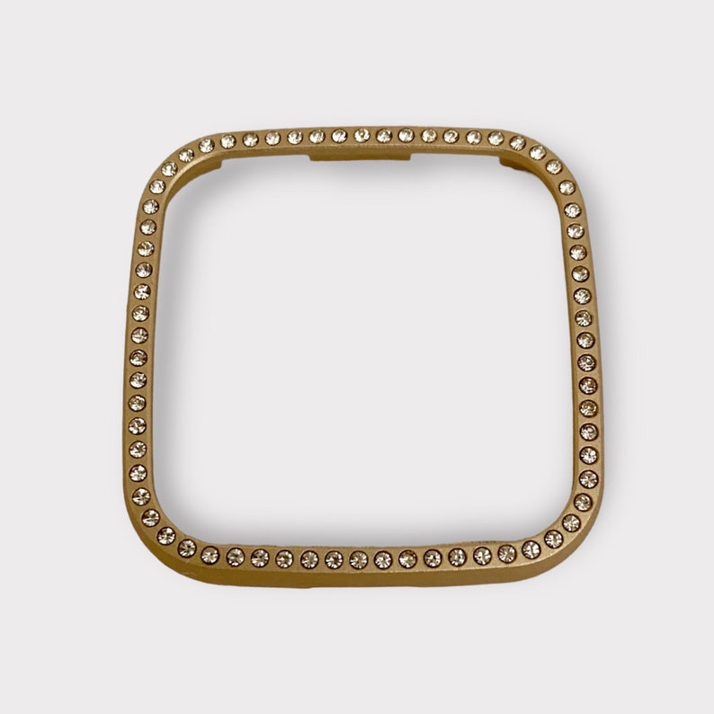 May include: Gold-toned square watch band with a clear crystal embellishment around the edge.