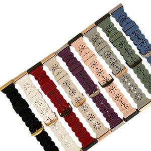 May include: A collection of colorful watch bands in various shades, including black, white, red, purple, pink, gray, green, and blue. Each band features a floral cutout design and a metal buckle. The bands are made of a flexible material.