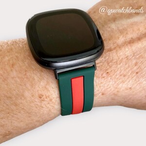 May include: A black smartwatch with a green and red silicone band. The band has a red stripe in the center and green stripes on either side.