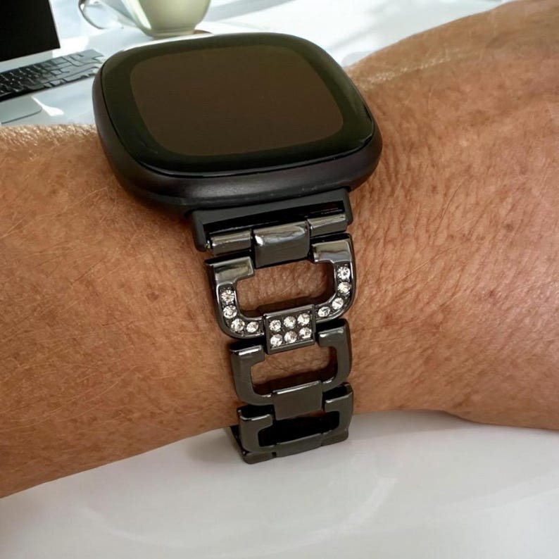 May include: Black metal watch band with clear rhinestones. The band is designed for a smartwatch with a square face.