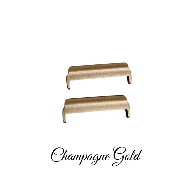 May include: Two gold-toned metal watch band strap adapters. The adapters are rectangular with rounded edges. The text "Champagne Gold" is written below the adapters.