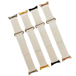 May include: Four white Apple Watch bands with different colored metal clasps. The bands are made of a flexible, ribbed material. The clasps are gold, rose gold, silver, and black.