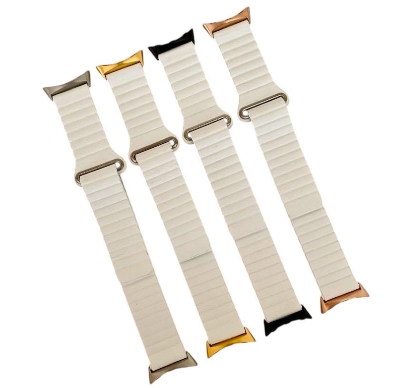 May include: Four white Apple Watch bands with different colored metal clasps. The bands are made of a flexible, ribbed material. The clasps are gold, rose gold, silver, and black.