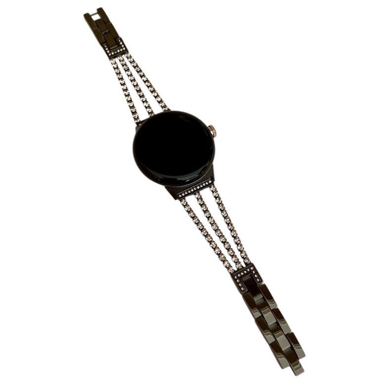 Pu&ograve; includere: Un orologio nero con quadrante nero e cinturino a catena argentato con strass.