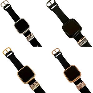 May include: Four different colored Apple Watch bands with decorative charms. The bands are black and the charms are silver, gold, and rose gold.