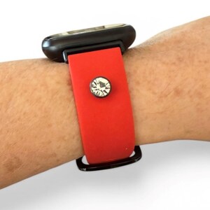 Peut inclure: Un bracelet de montre rouge avec un cadran noir. Le bracelet est orn&eacute; d'un accent scintillant, rond, en forme de cristal. La montre est pr&eacute;sent&eacute;e sur un poignet.