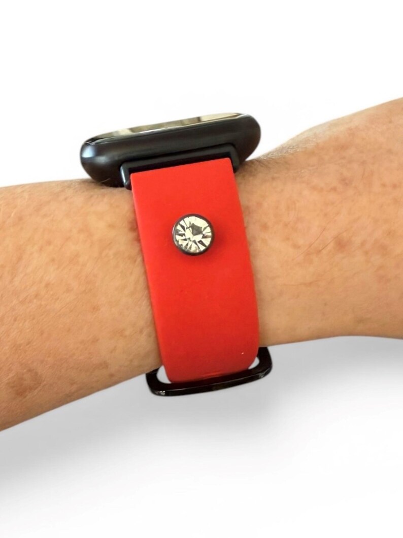 Peut inclure: Un bracelet de montre rouge avec un cadran noir. Le bracelet est orn&eacute; d'un accent scintillant, rond, en forme de cristal. La montre est pr&eacute;sent&eacute;e sur un poignet.