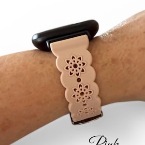May include: A light pink watch band with a floral design. The band is attached to a black watch face. The word "Pink" is written in cursive at the bottom of the image.