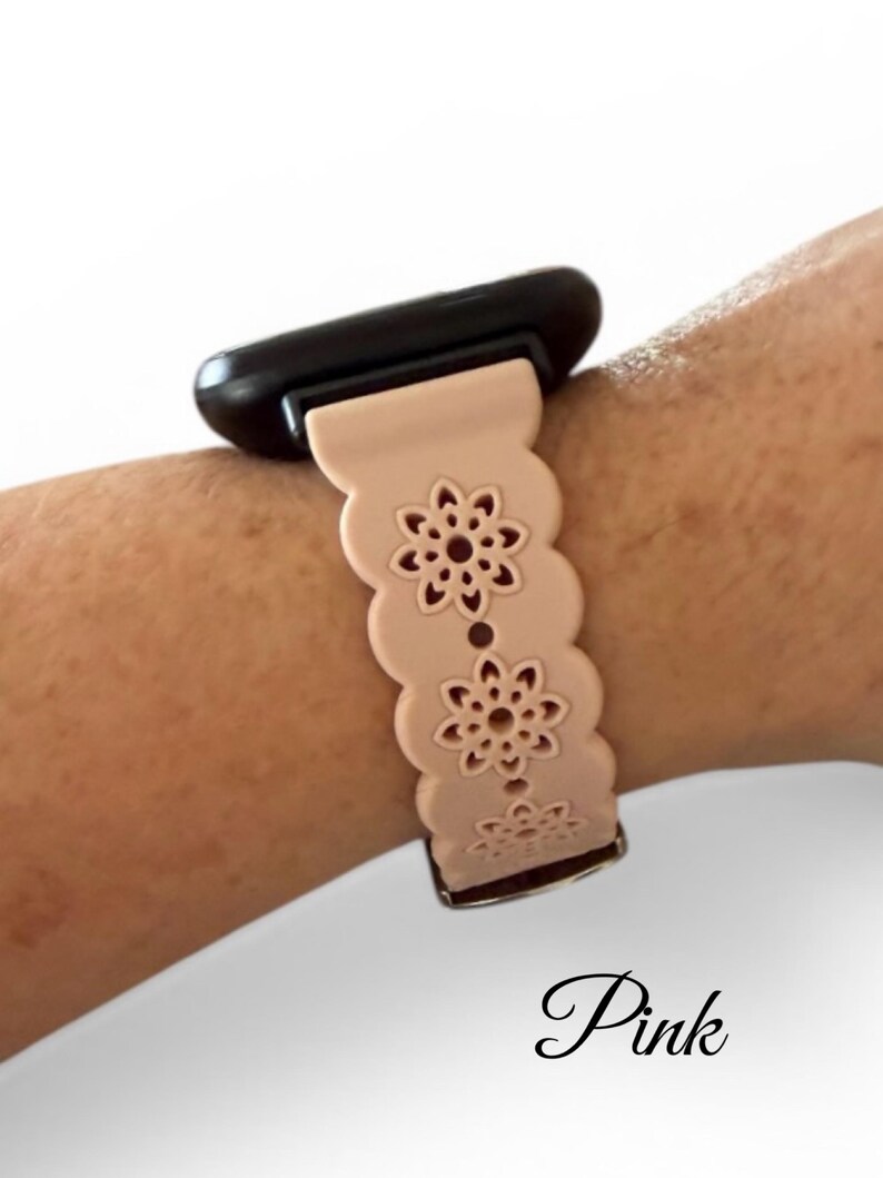 May include: A light pink watch band with a floral design. The band is attached to a black watch face. The word "Pink" is written in cursive at the bottom of the image.